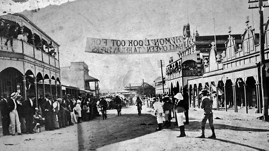 An image from 1908 of the main street of Ravenswood with cyclists rising underneath a Halloween banner.