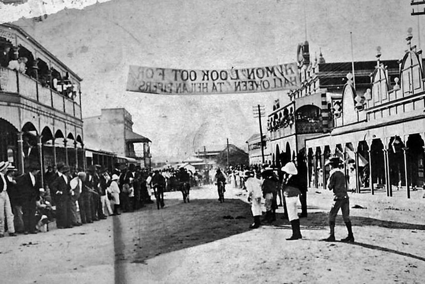 An image from 1908 of the main street of Ravenswood with cyclists rising underneath a Halloween banner.