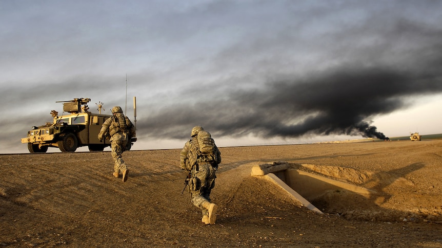 Shot from a low angle, US soldiers run up a road embankment to an army Hummer as black smoke rises from the horizon.
