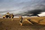 Shot from a low angle, US soldiers run up a road embankment to an army Hummer as black smoke rises from the horizon.