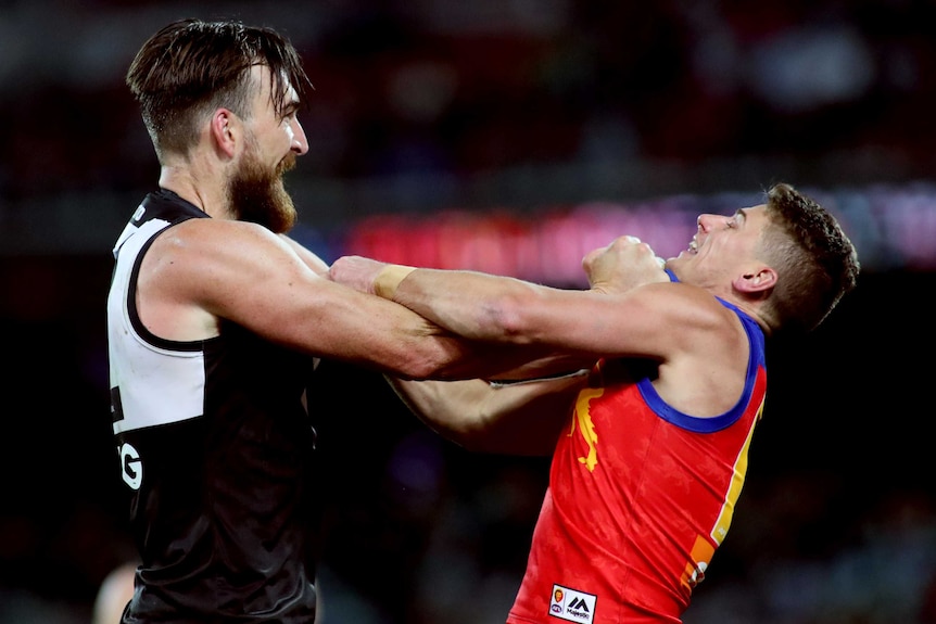 Two AFL players hold each other by the top of their jerseys as they get involved in a scuffle.