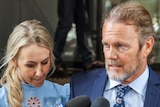 Craig McLachlan addresses the media outside a Sydney building with partner Vanessa Scammell beside him.