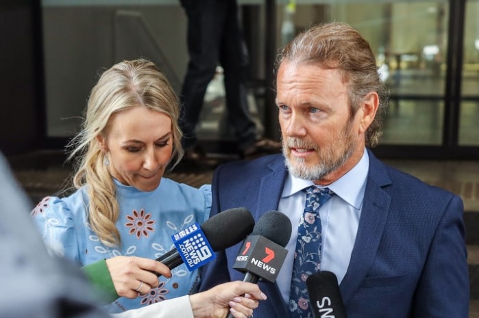 Craig McLachlan addresses the media outside a Sydney building with partner Vanessa Scammell beside him.