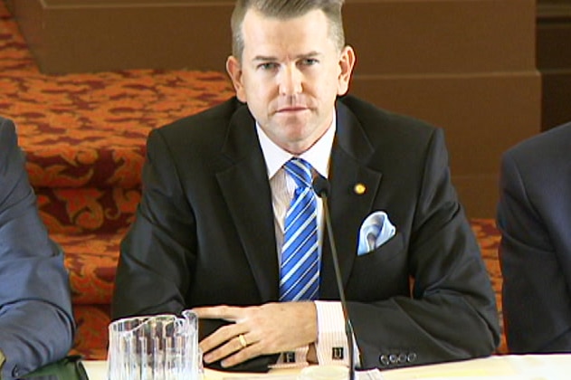 Jarrod Bleijie sits at a desk with his arms crossed that show him wearing 'FU' cufflinks.