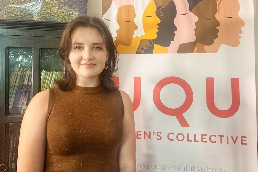 Emily smiles next to a UQ Women's Collective banner.