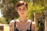A woman with short hair and arm tattoos smiles for a photo
