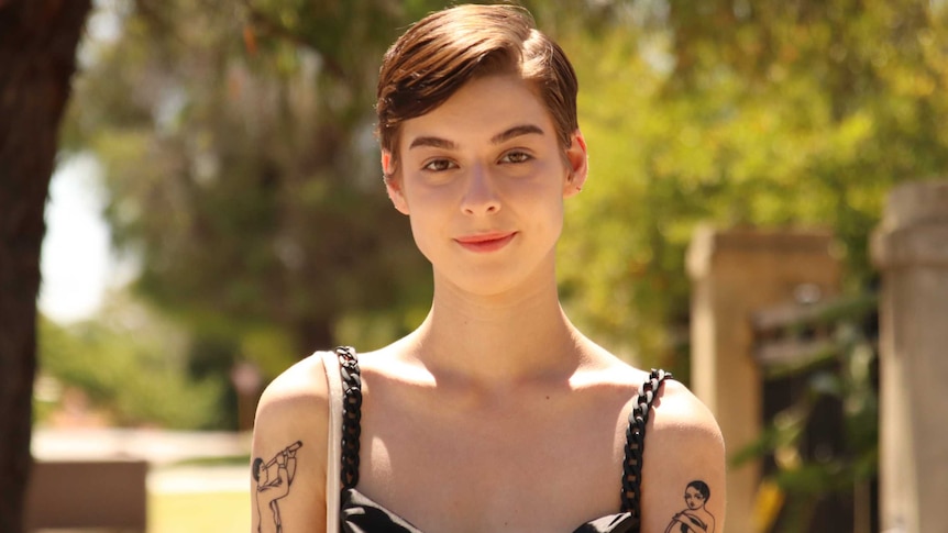 A woman with short hair and arm tattoos smiles for a photo