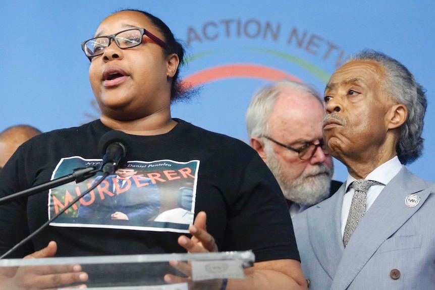 Emerald Garner wears a t-shirt with a picture of a policeman and murderer written across it as she speaks at a press conference.
