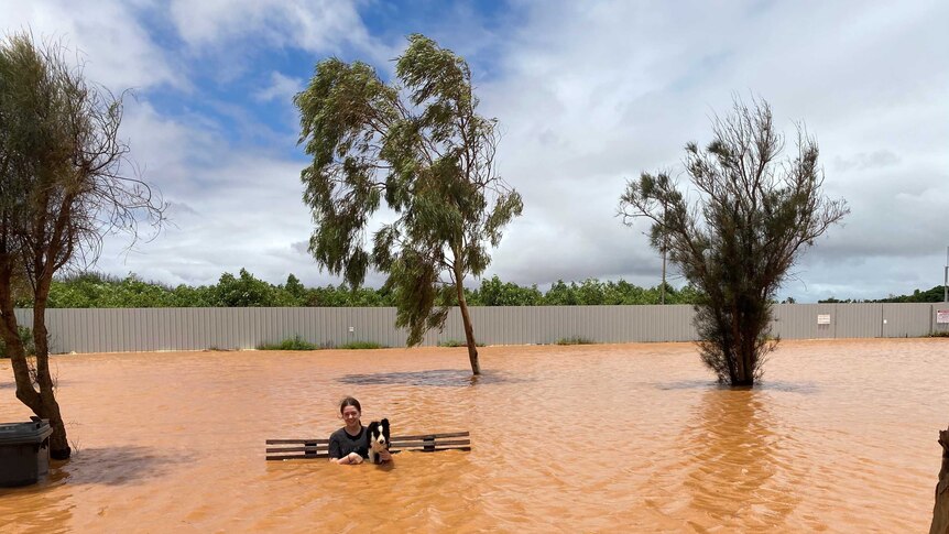 A woman sits on a bench with a dog in flooded water.