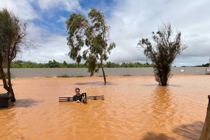 A woman sits on a bench with a dog in flooded water.