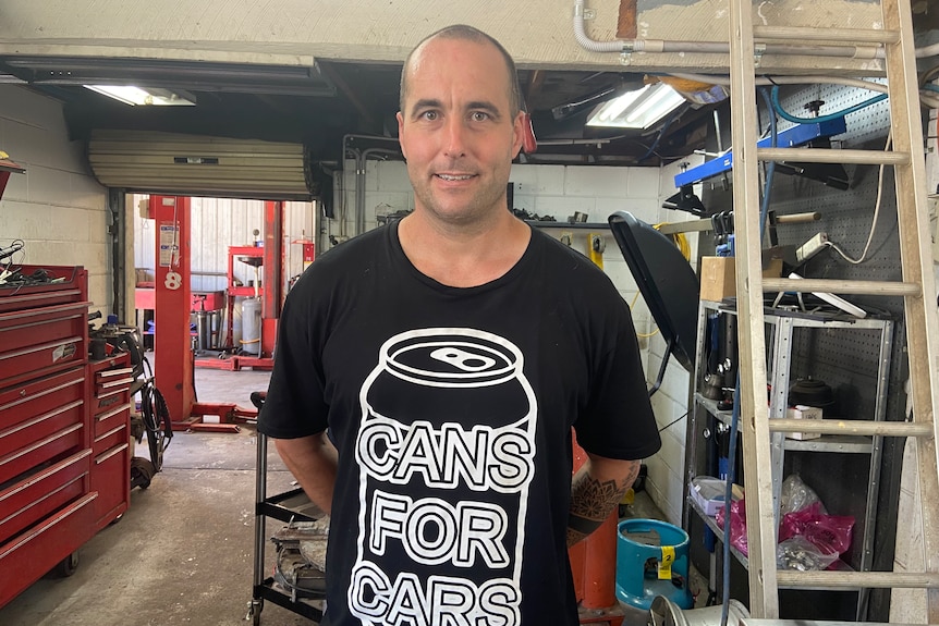 Sam Tucker stands in mechanics workshop wearing 'Cans for Cars' tshirt