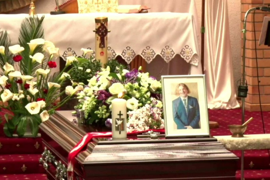 A coffin with flowers and a photo on top.