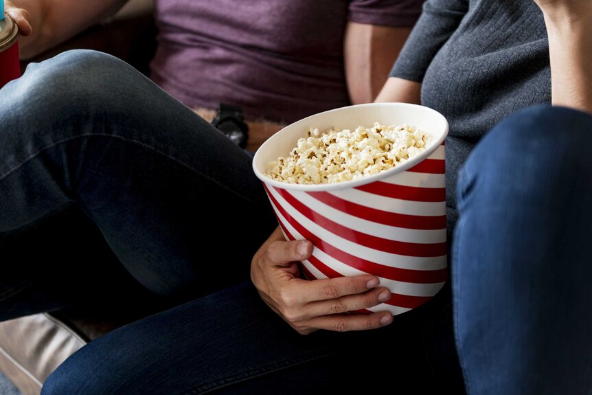 Two people eat popcorn on a couch.