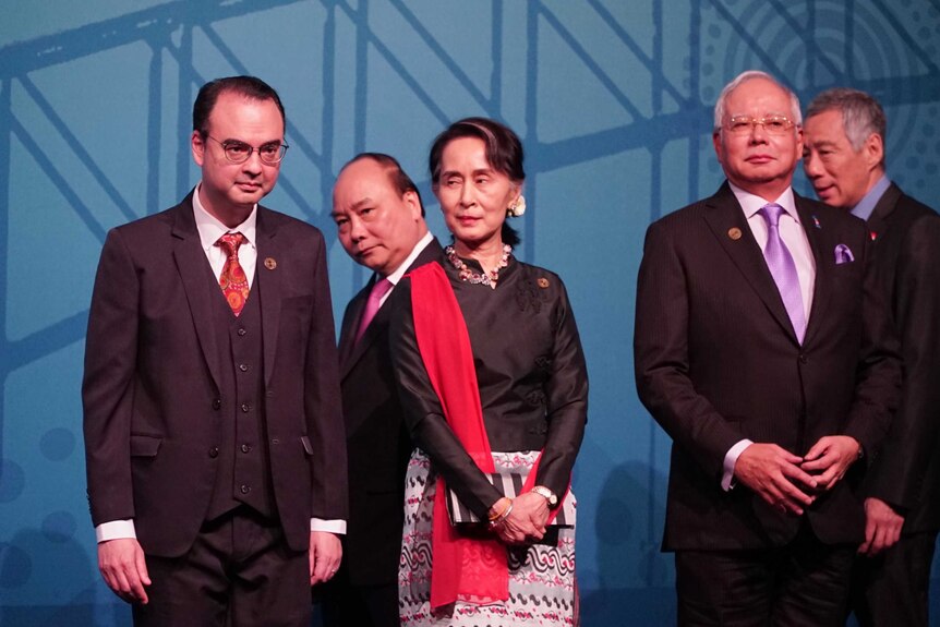 Politicians at ASEAN summit stand in a line in front of blue background.