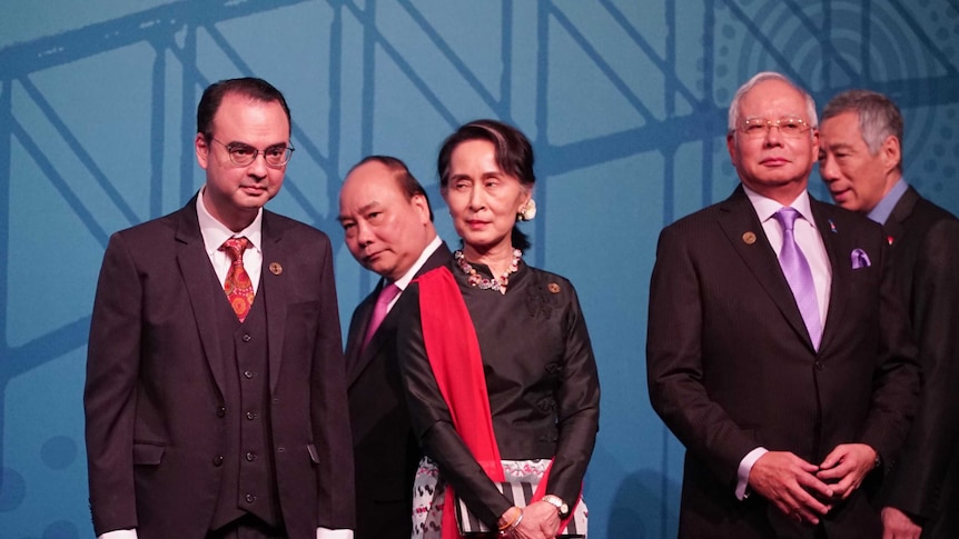 Politicians at ASEAN summit stand in a line in front of blue background.
