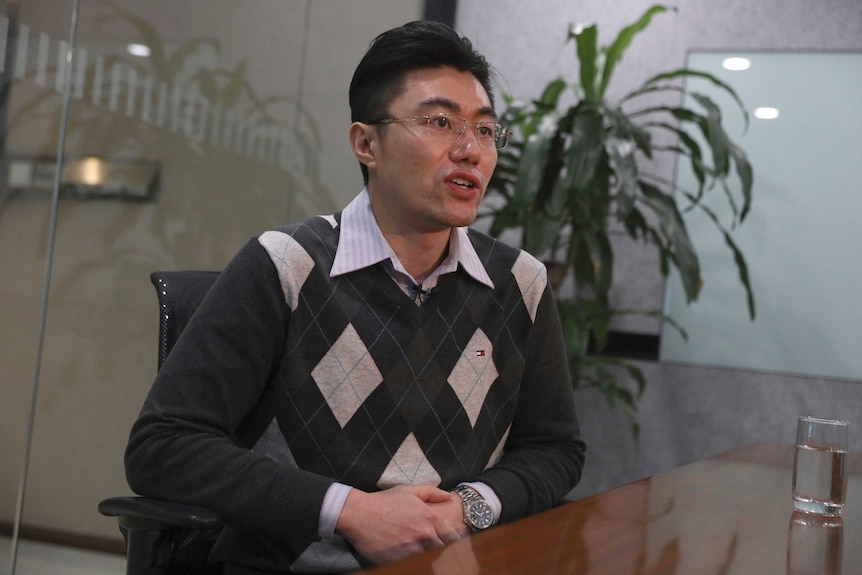 A man wearing classes and wearing a shirt and vest facing right inside an office.