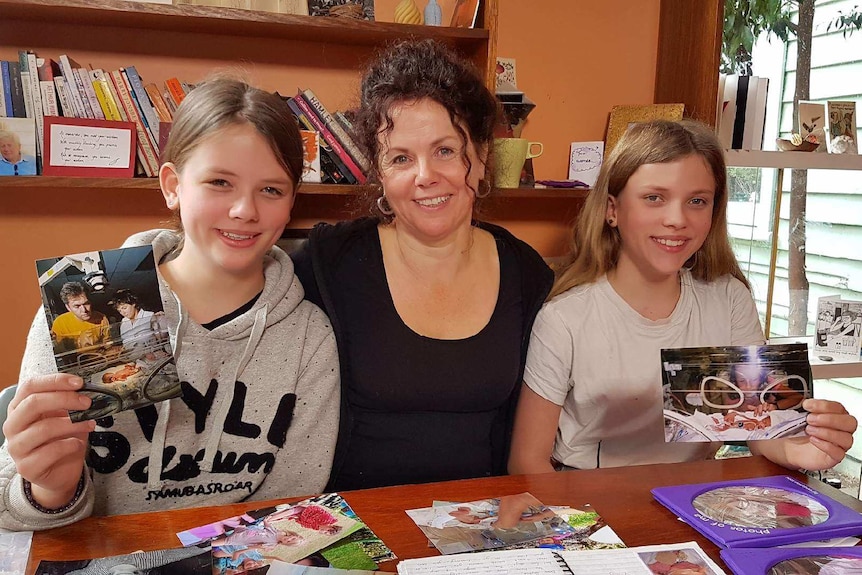 Sophie and Tilly with their mum. The girls are holding photos of them as newborns.