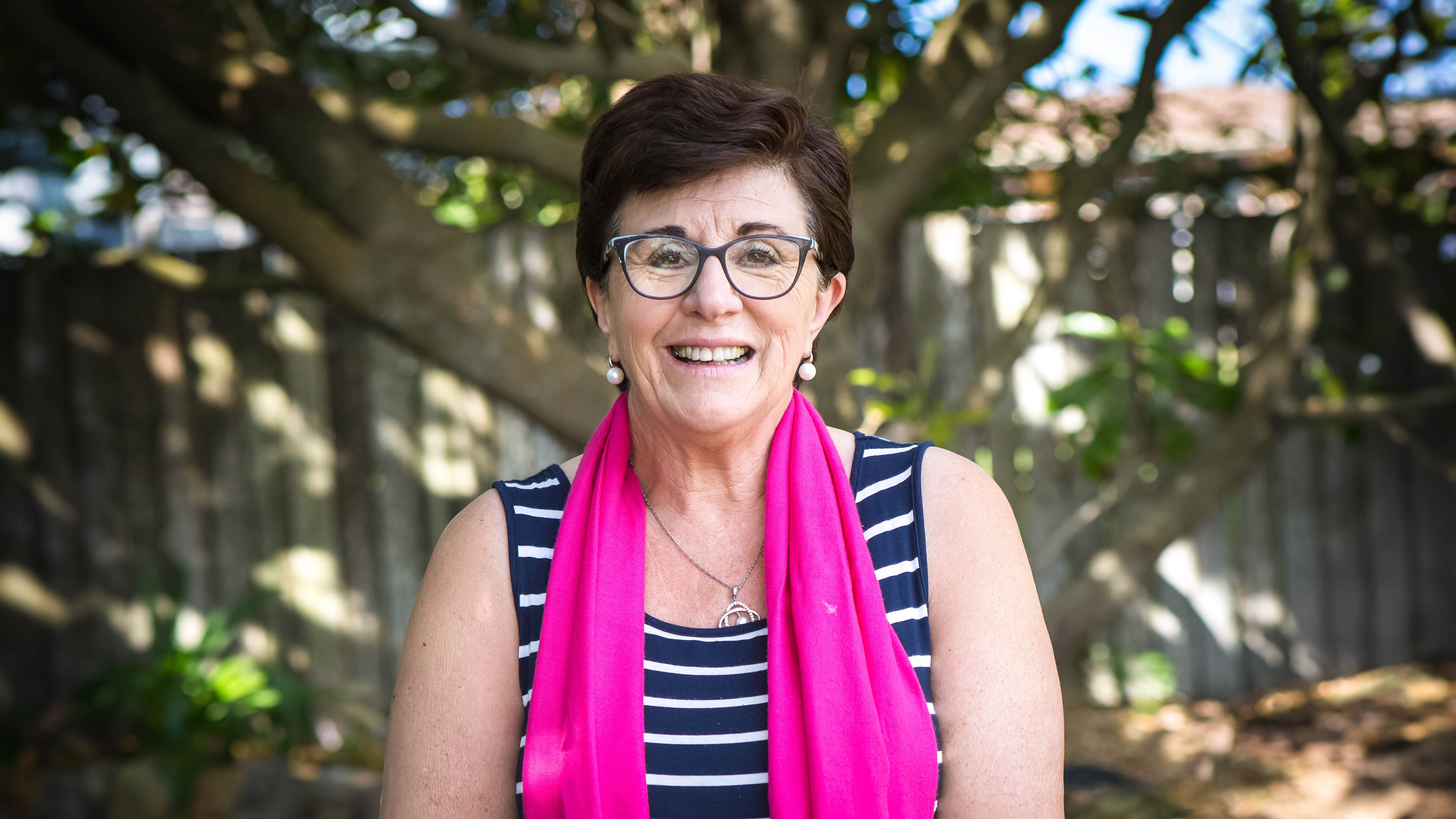 A woman with glasses and a vibrant scarf smiles with joy