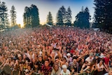 Crowds front a festival stage at sunset