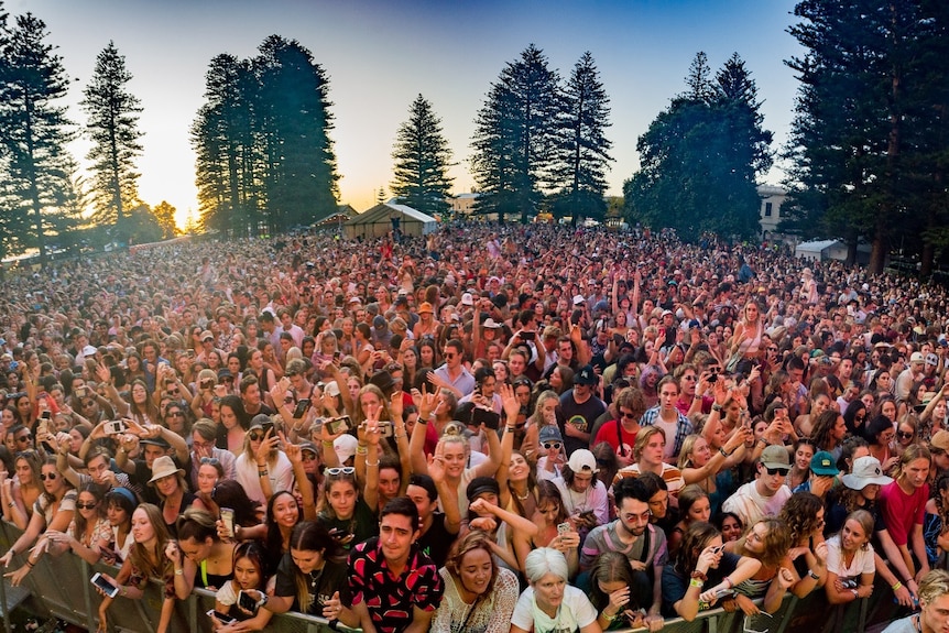 Crowds front a festival stage at sunset