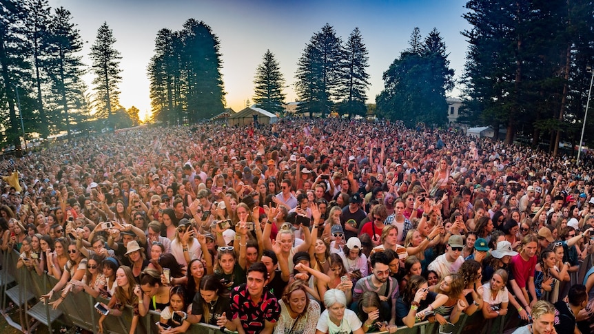 Crowds front a festival stage at sunset
