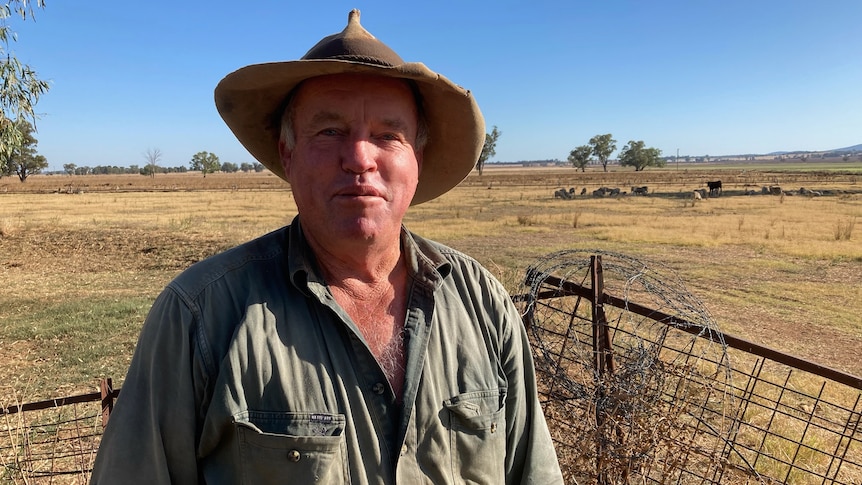 A middle aged man wearing an akubra standing in a field.
