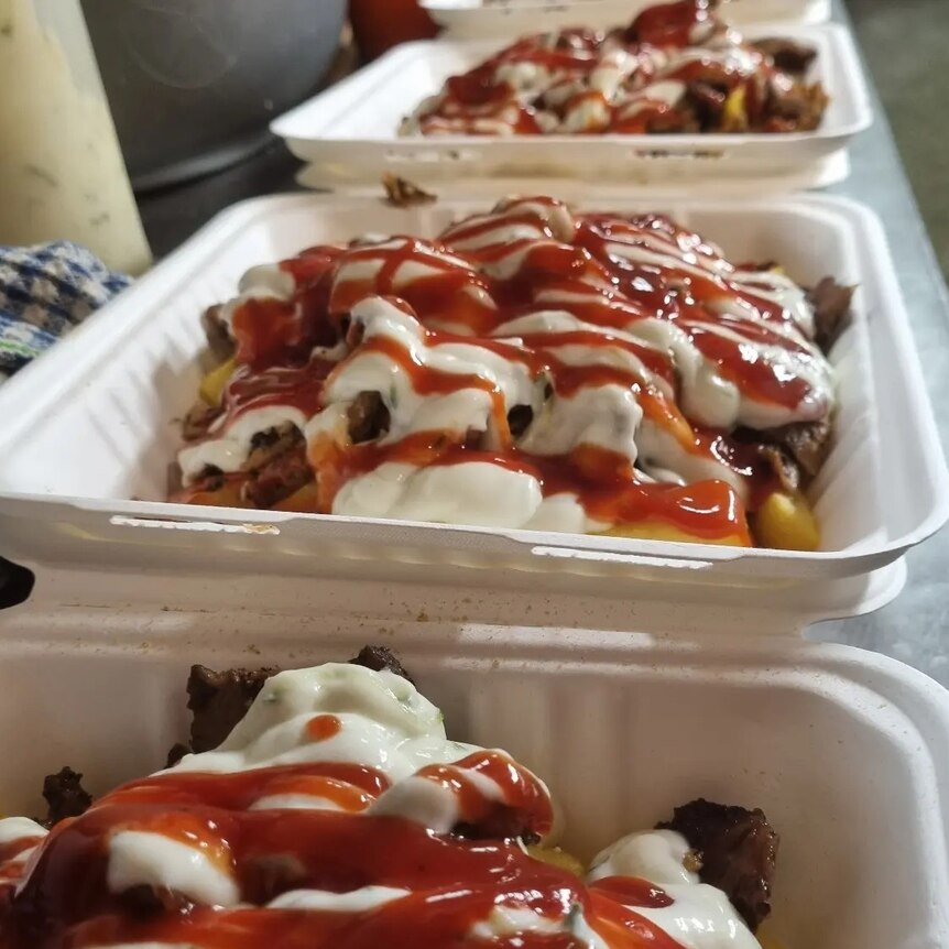 styrofoam trays with meat and chips covered in white sauce and red sauce
