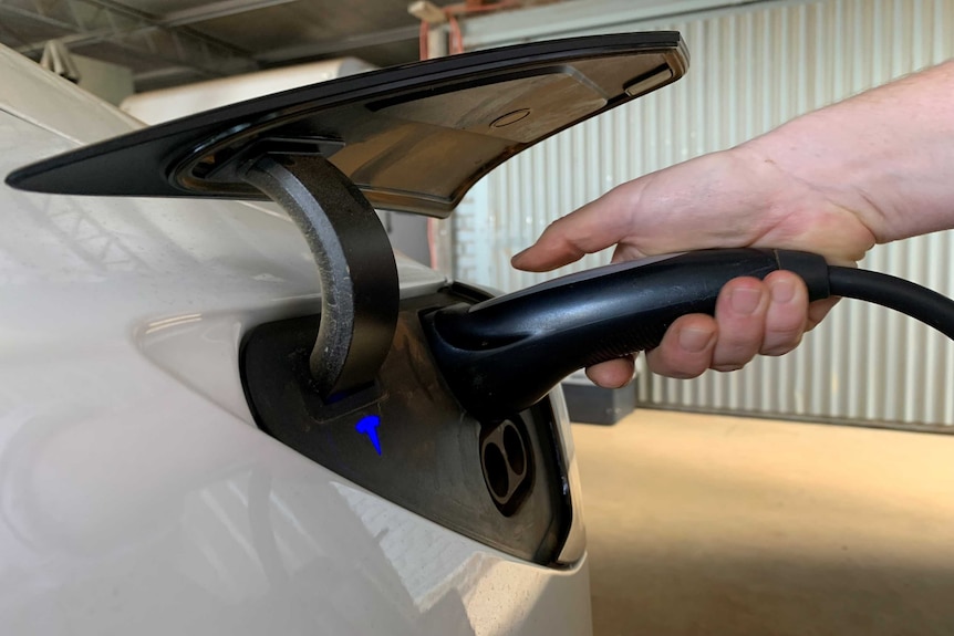 A hand holding an electric vehicle charger and plugging it into the car.