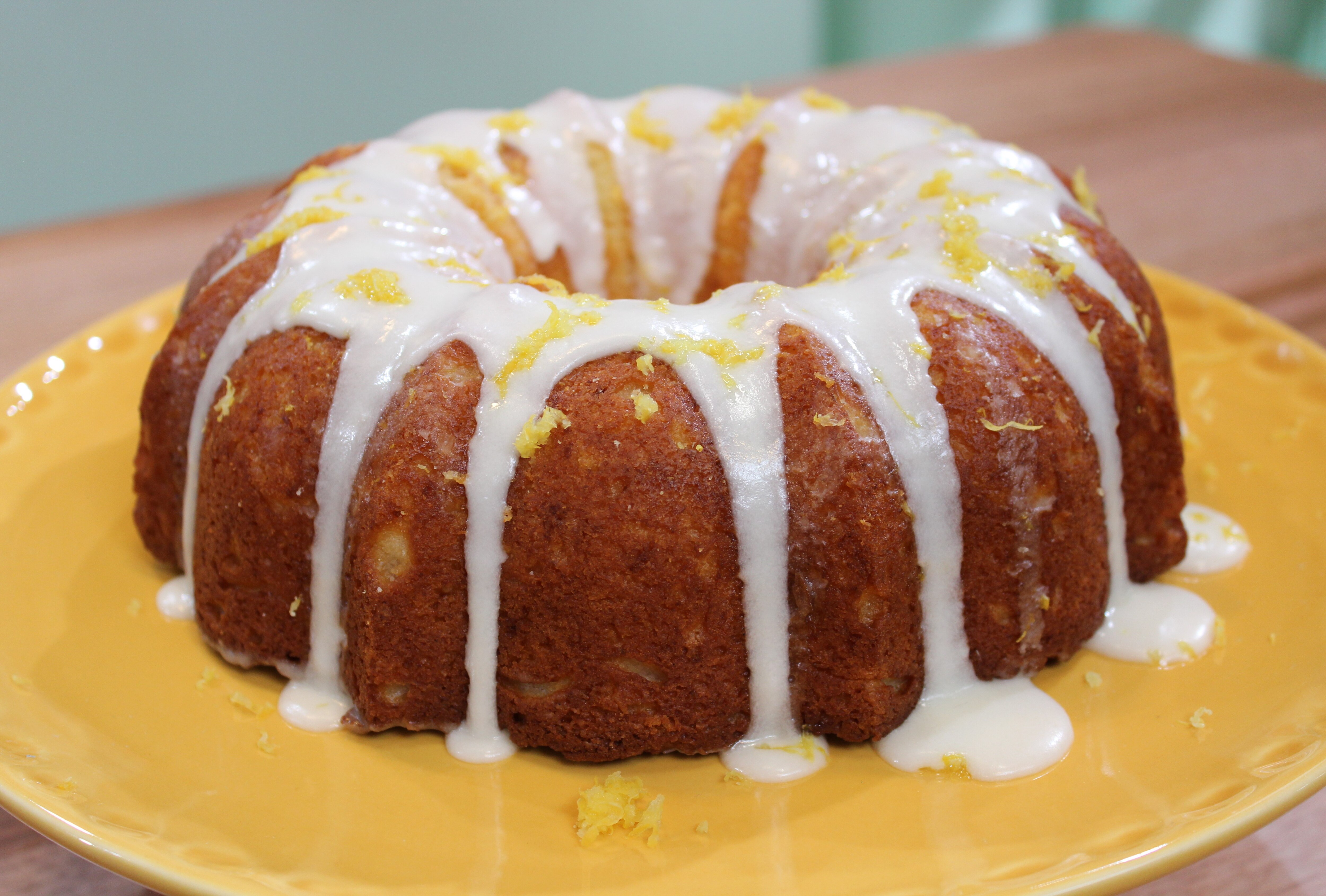 A picture of a lemon and ricotta cheesecake iced with icing dripping down the sides, sitting on a plate.