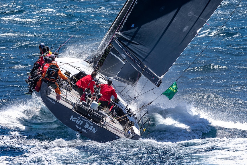 Crew members in red jackets sit on a yacht deck at sea during a race