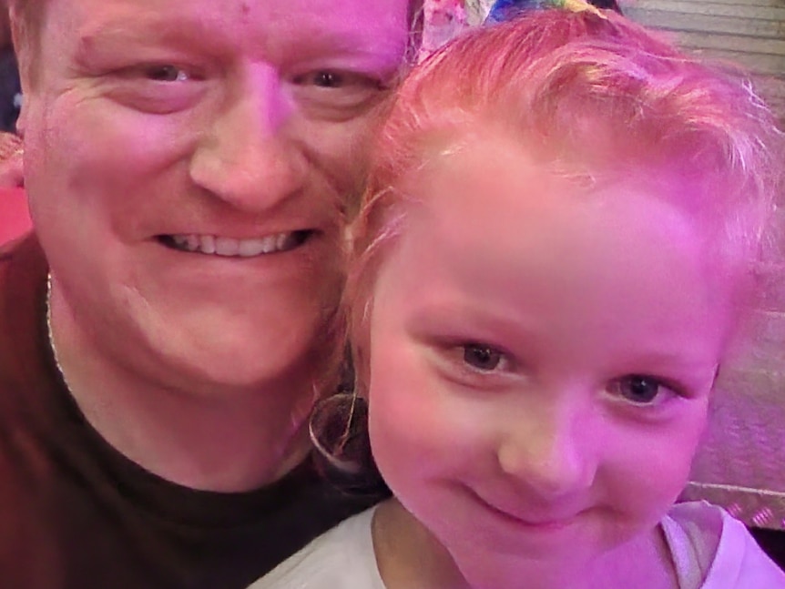 A smiling man huddles with his young daughter for a selfie.