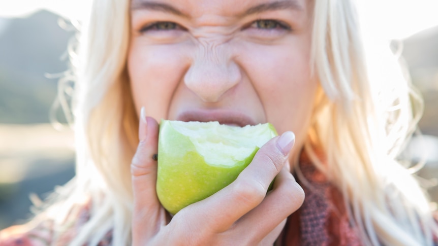 woman with blonde hair eating an apple close up