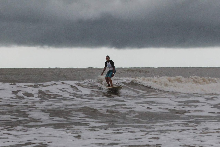a surfer on long board with storm clouds and small waves
