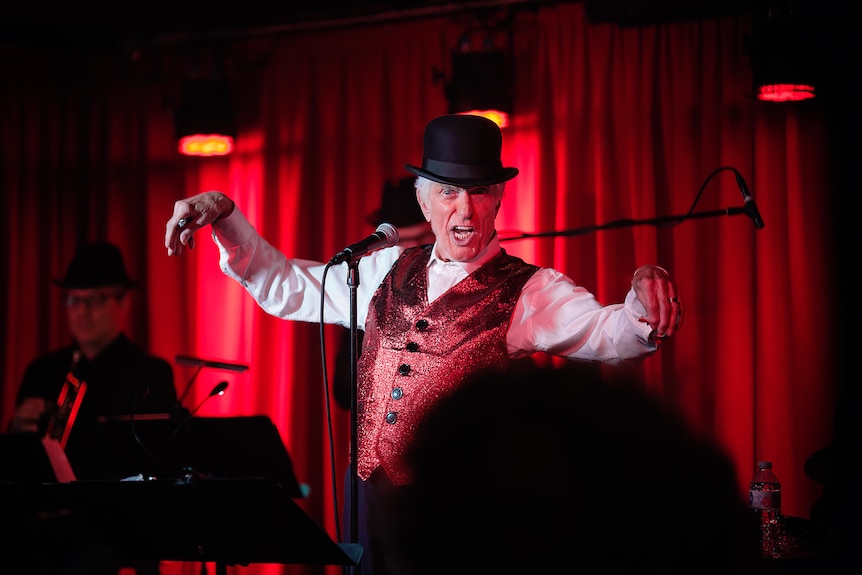 A man in a bowler hat and red vest performs on stage