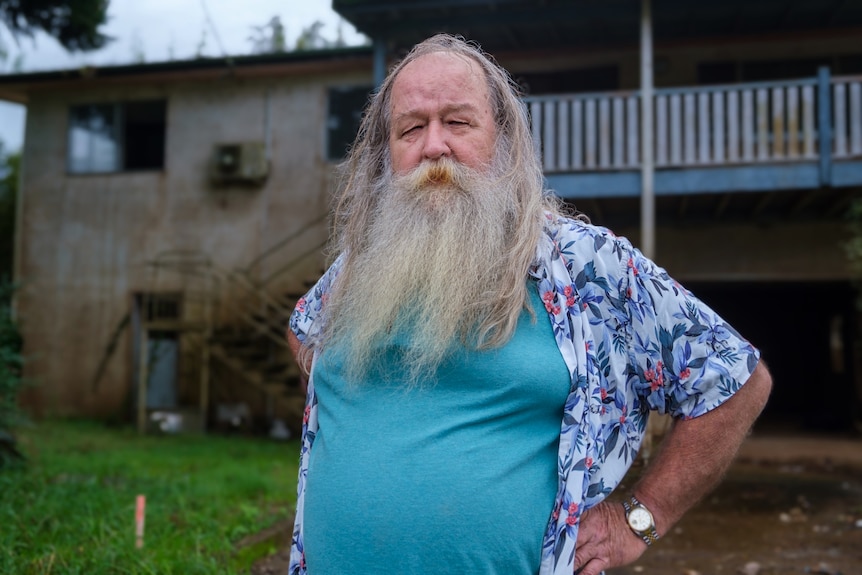 Un hombre con una larga barba gris que lleva una camisa floral sobre una camiseta azul.