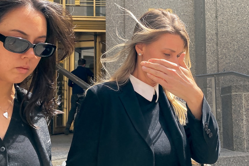 a woman walking out of a courthouse covers her face with her hands 