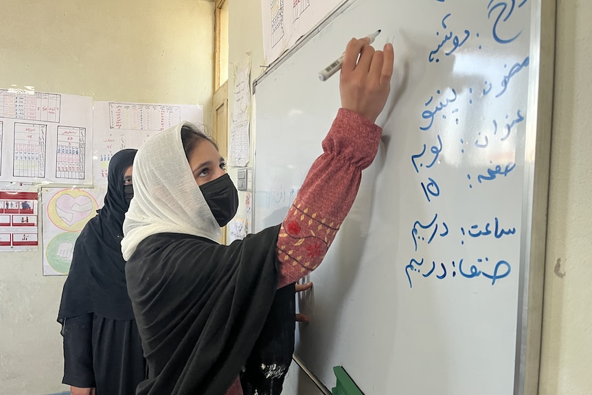 A girl in mask and hijab writing on white board.