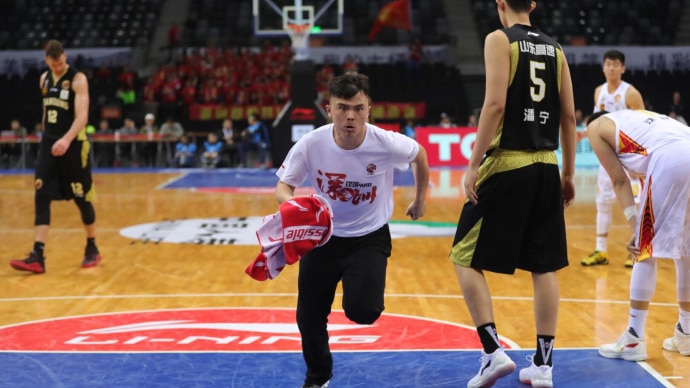 Meng Fei runs onto a basketball court, he is holding a red towel.