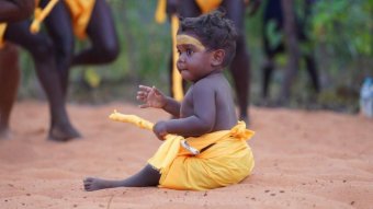 A baby sitting in the Garma 2019 opening ceremony in traditional costume.