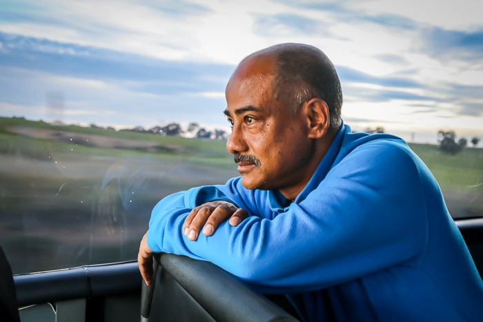 A man sitting up on a bus seat, with the Australian landscape visible from the window.