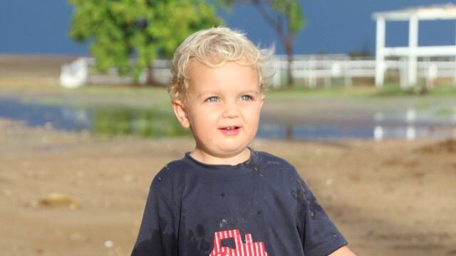 A toddler and his dog in the rain on a property in western Queensland.