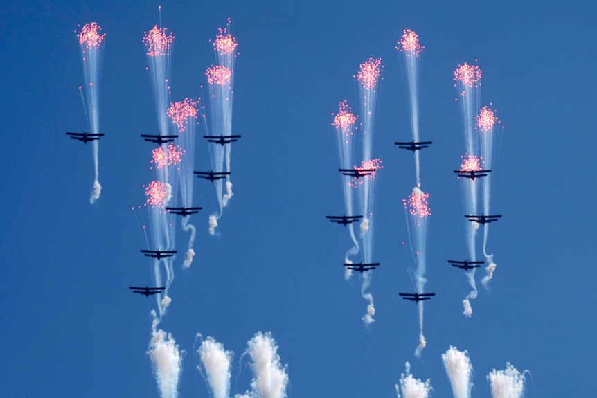 Airplanes forming the number 70 fly in formation and fire flares.