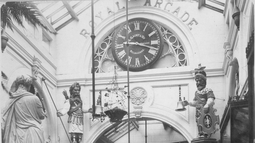 A black and white photo of Royal Arcade interior, with ornate clock and statues in background.