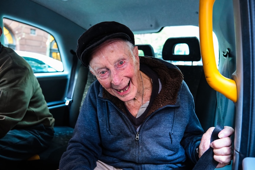An older man smiles in a taxi on Anzac Day.