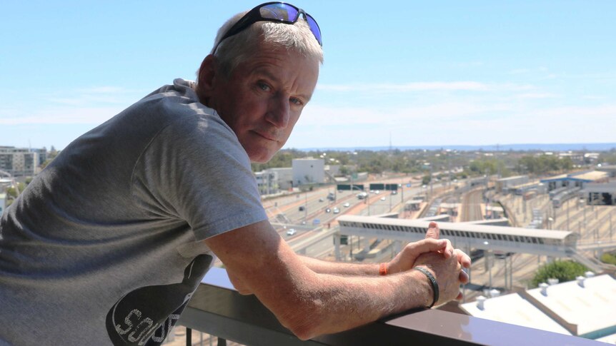 Ian, a homeless man who has taken part in a running program, leans on the edge of a balcony in East Perth.