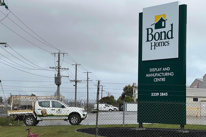 A large green sign behind a fence in a car park that reads "Bond Homes".