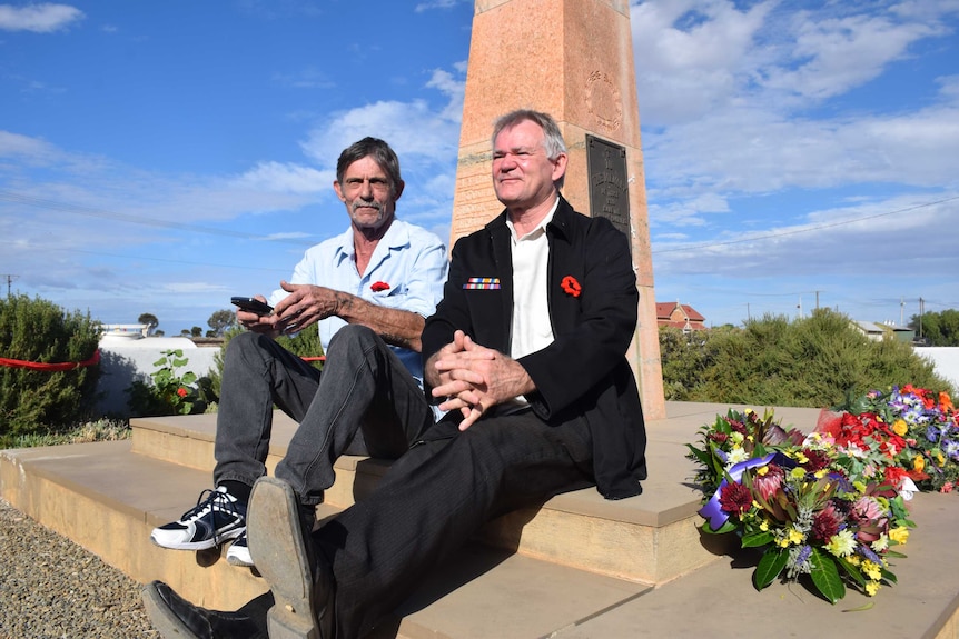Two men sit on a the base of a war memorial.