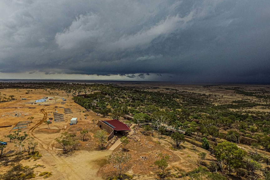 A drone shot shows dark clouds rolling in across the sky over the outback landscape.