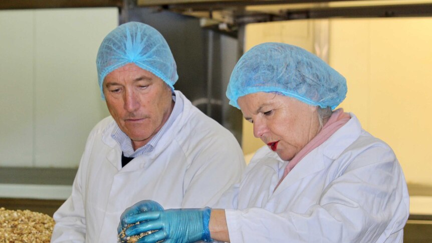 A man and woman in a factory wearing white coats and hair nets inspect a batch of muesli