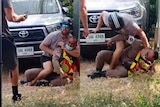 Composite photo of two men scuffling on the ground in front of car 